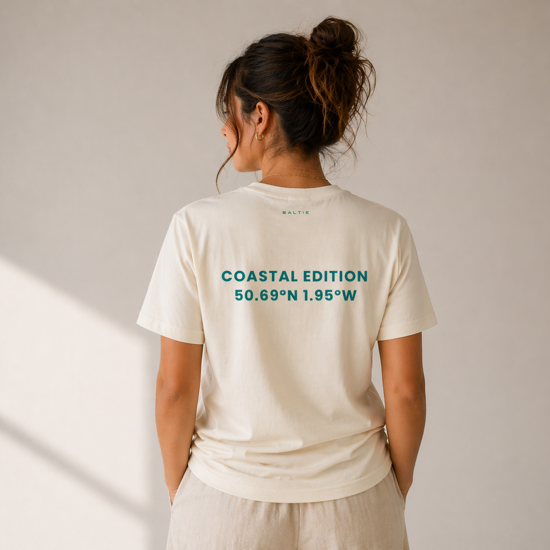 Person wearing a white t-shirt with 'Coastal Edition' text on the back against a plain background