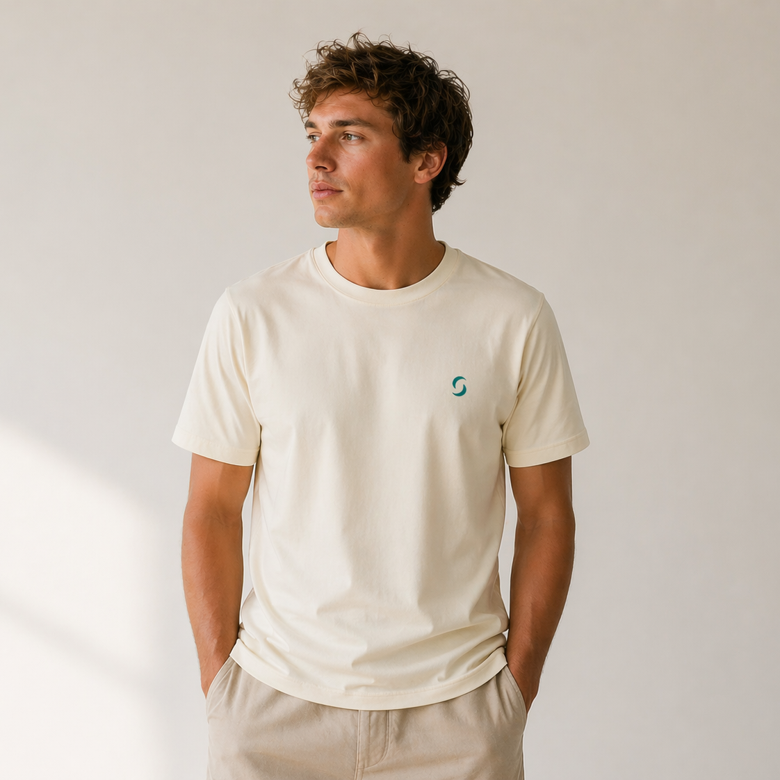 Man wearing a beige t-shirt with a small logo on a plain background