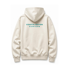 A branded saltie hoodie against a white background the main colour is beige and the logo on the back reads "coastal edition" in a teal colour.