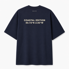 A navy blue shirt against a white background, That says coastal edition on the back of it in a beige colour.