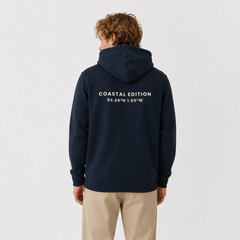 Person wearing a navy hoodie with 'Coastal Edition' text on the back, standing against a light gray background.