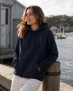 Person wearing a navy hoodie with a logo, standing by a waterfront.