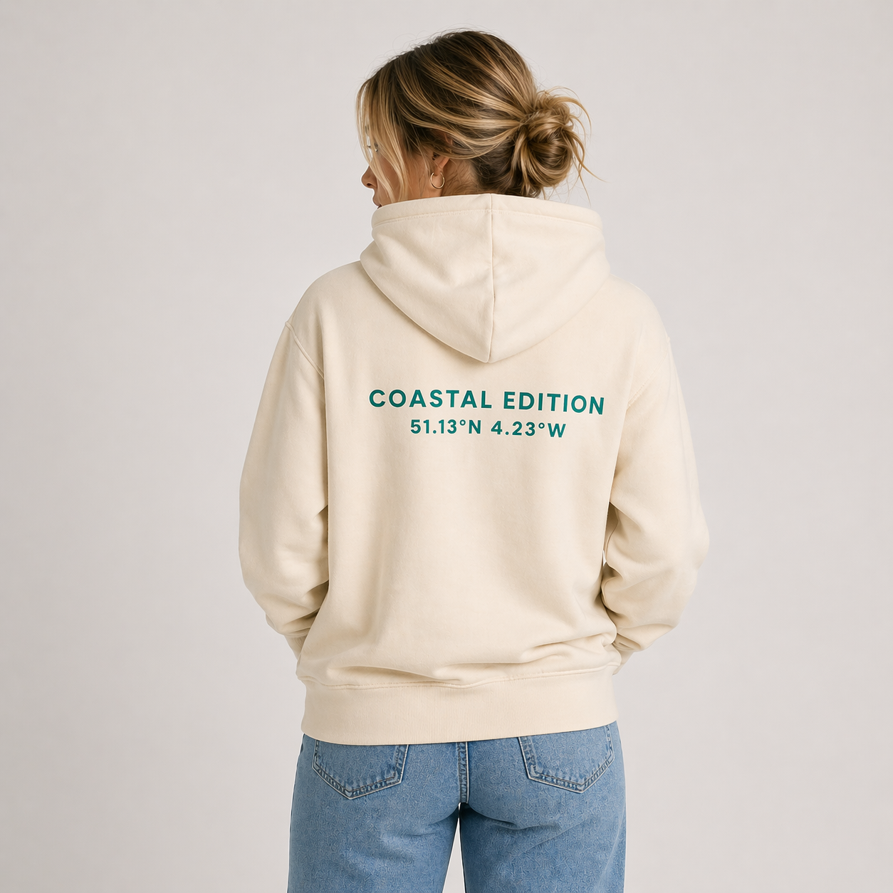 A woman facing away from the camera wearing a Biege hoodie. The woman is against a white background and the text reads 