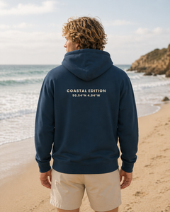 Person wearing a navy hoodie with 'Coastal Edition' text on the beach