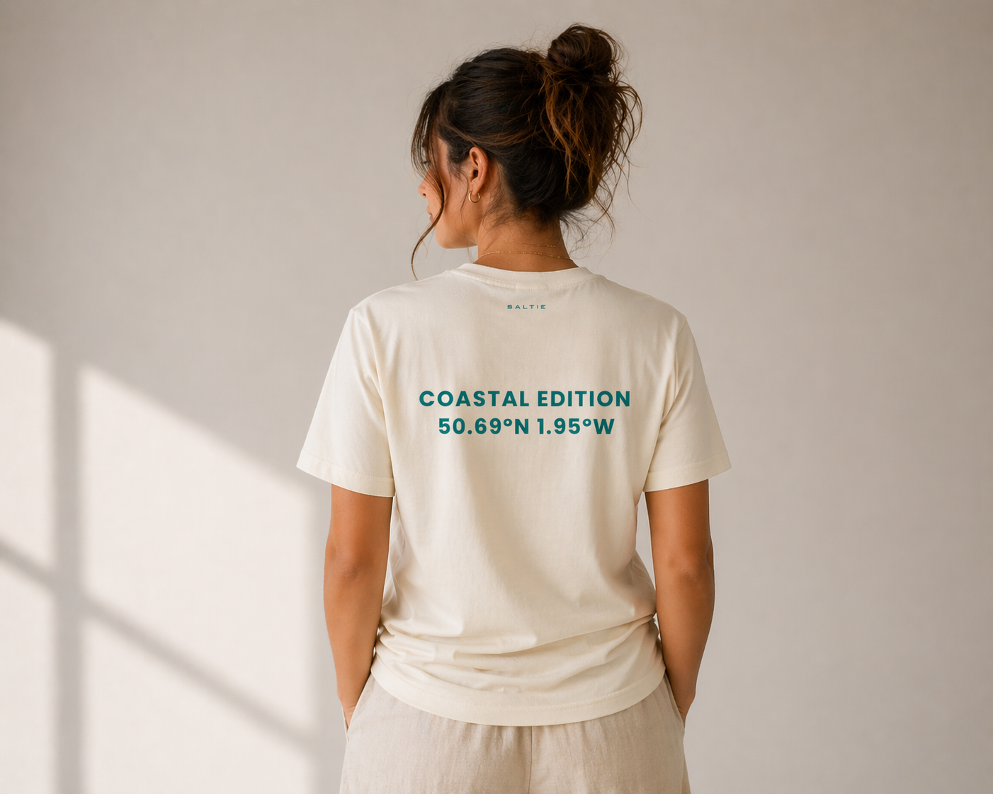 Person wearing a white t-shirt with 'Coastal Edition' text on the back against a plain background