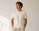 Man wearing a beige t-shirt with a small logo on a plain background