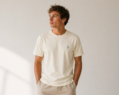 Man wearing a beige t-shirt with a small logo on a plain background