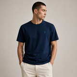 Man wearing a navy blue t-shirt with a small logo on a beige background