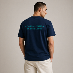 Man wearing a navy blue t-shirt with 'Coastal Edition' text on the back, standing against a beige background.