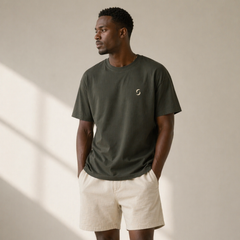 Man wearing a green t-shirt with a logo and beige shorts against a neutral background